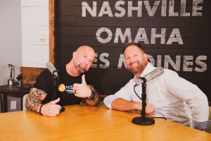 two guys sitting at a table doing a podcast show