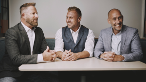 three middle aged men dressed in suits sitting on the same side of the table