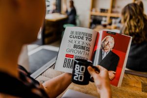 a man holding a cup of coffee and reading a book about entrepreneurship