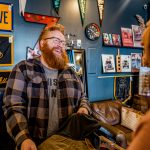 a man with a red beard and a flannel helps a customer purchase clothing at a men's store in omaha.