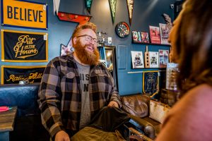 a man with a red beard and a flannel helps a customer purchase clothing at a men's store in omaha. 