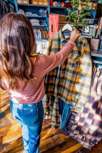 A dark haired women in blue jeans and a top shops for a flannel in a men's store in omaha. 