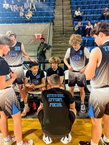 a group of AAU basketball players in a huddle listening to their coach. 