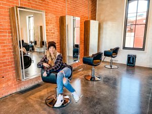 a women in jeans and a flannel shirt sitting in a salon chair