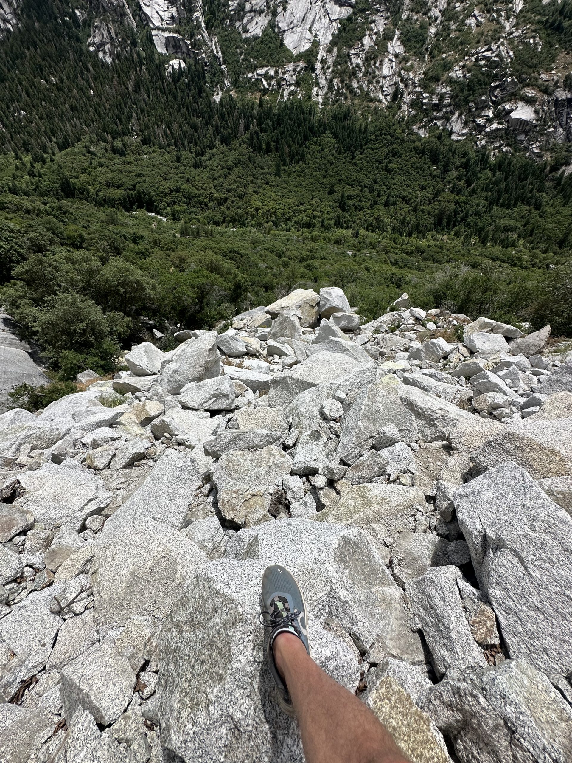 a foot of a hiker cautiously assessing the very steep descent of the boulders on a mountain side. 