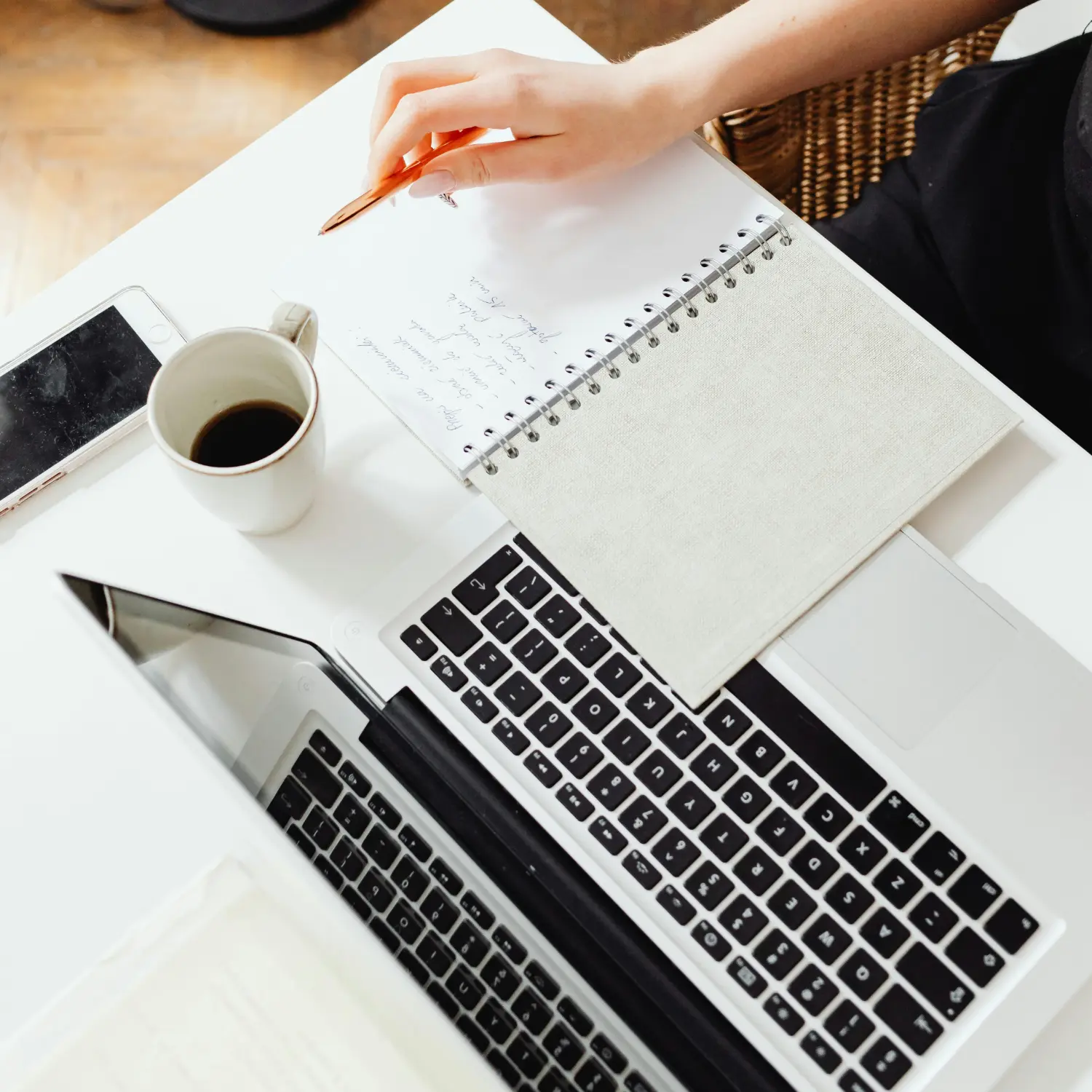 A person writing in a notebook next to a laptop.
